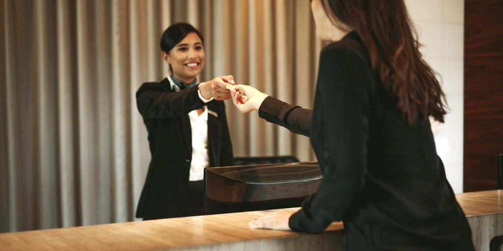 Female guest taking room key card at hotel check-in desk. Female receptionist giving room key to client in hotel.