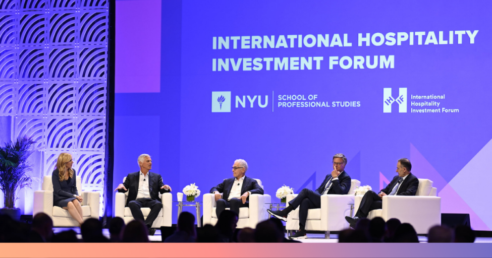 Five people sit on stage in white chairs, engaging in a panel discussion at the International Hospitality Investment Forum, with NYU School of Professional Studies branding displayed on a large purple screen behind them.