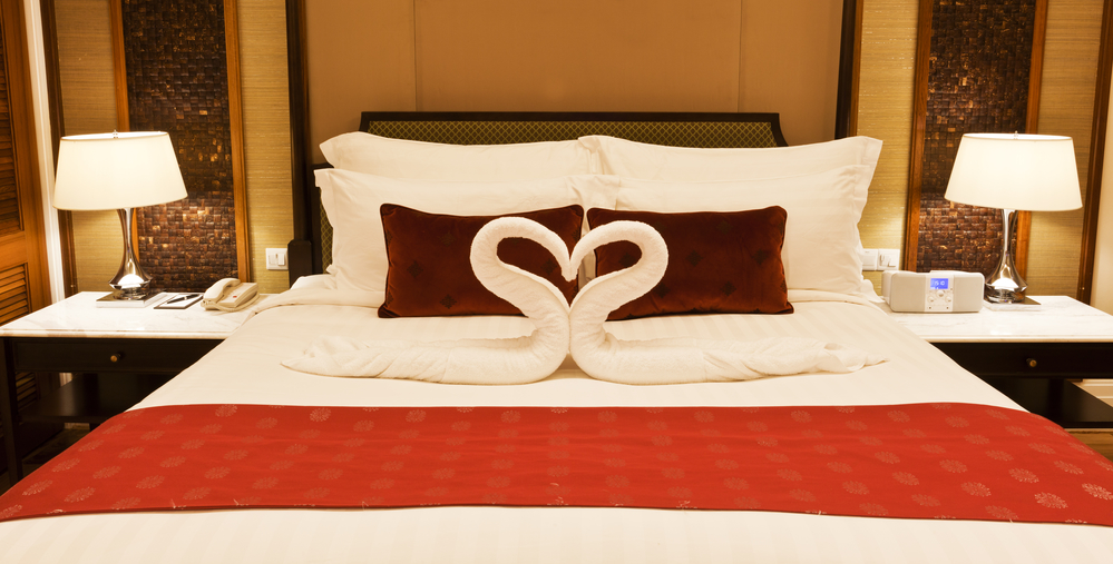 Bed in hotel room with towel forming heart shape